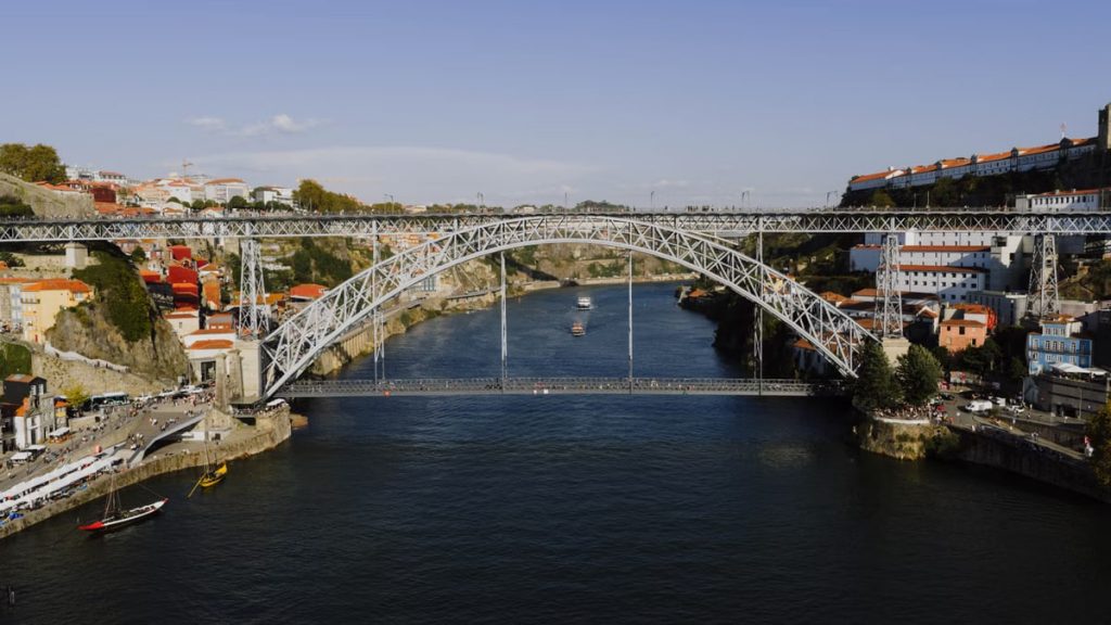 Capture of the iconic Dom Luís I Bridge spanning the Douro River in Porto, Portugal, under a vibrant day sky.